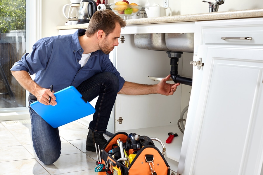 “A plumber conducting an inspection of sink pipes in a kitchen, ensuring proper functionality and identifying any potential issues