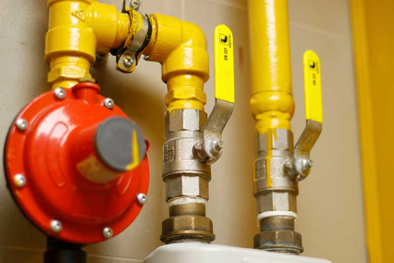 A row of yellow Gas industrial pipes with pressure gauges and valves connected to them.