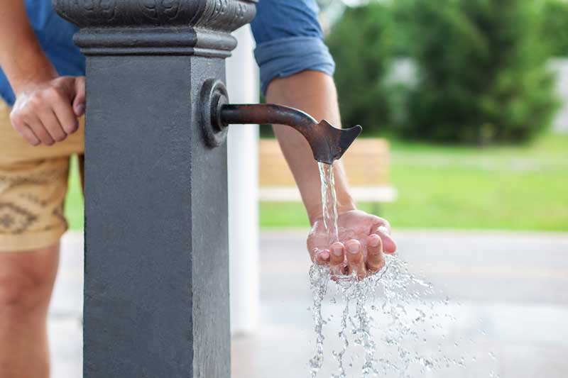 A man washing his hands with water from a water fountain.