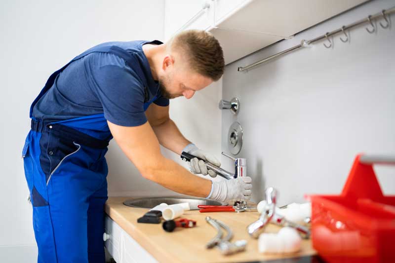 A man in overalls fixing a kitchen sink, demonstrating his handyman skills and expertise.