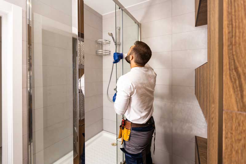 A man from Repipe Plumbing cleaning a shower in a bathroom.