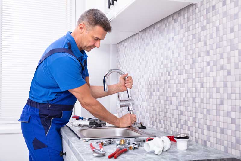 An experienced plumber fixing a kitchen sink, surrounded by plumbing equipment.