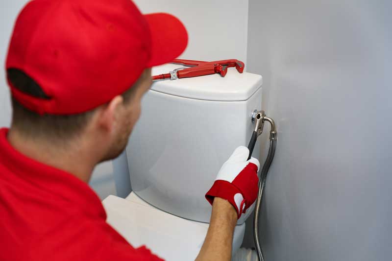 A man in a red shirt expertly fixing a toilet during a Toilet Installation & Repair task.