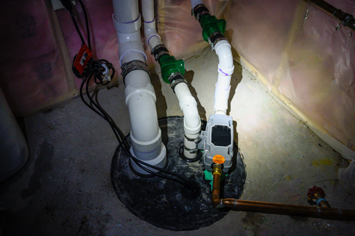 A sump pump and discharge pipe in a basement mechanical room.