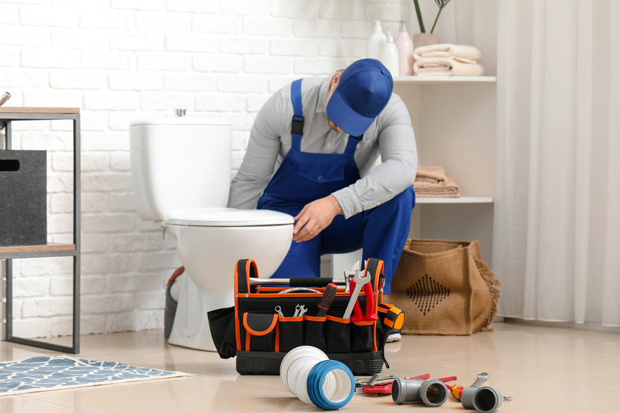 A professional plumber fixing a toilet in a bathroom, with tools and equipment ready for the job
