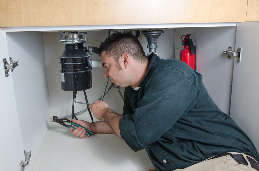 Plumber installing a garbage disposal unit under a kitchen sink