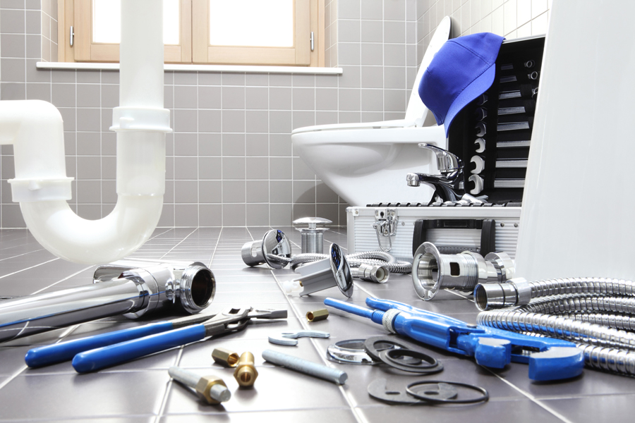 Plumbing tools and parts arranged on a bathroom floor, ready for installation or repair